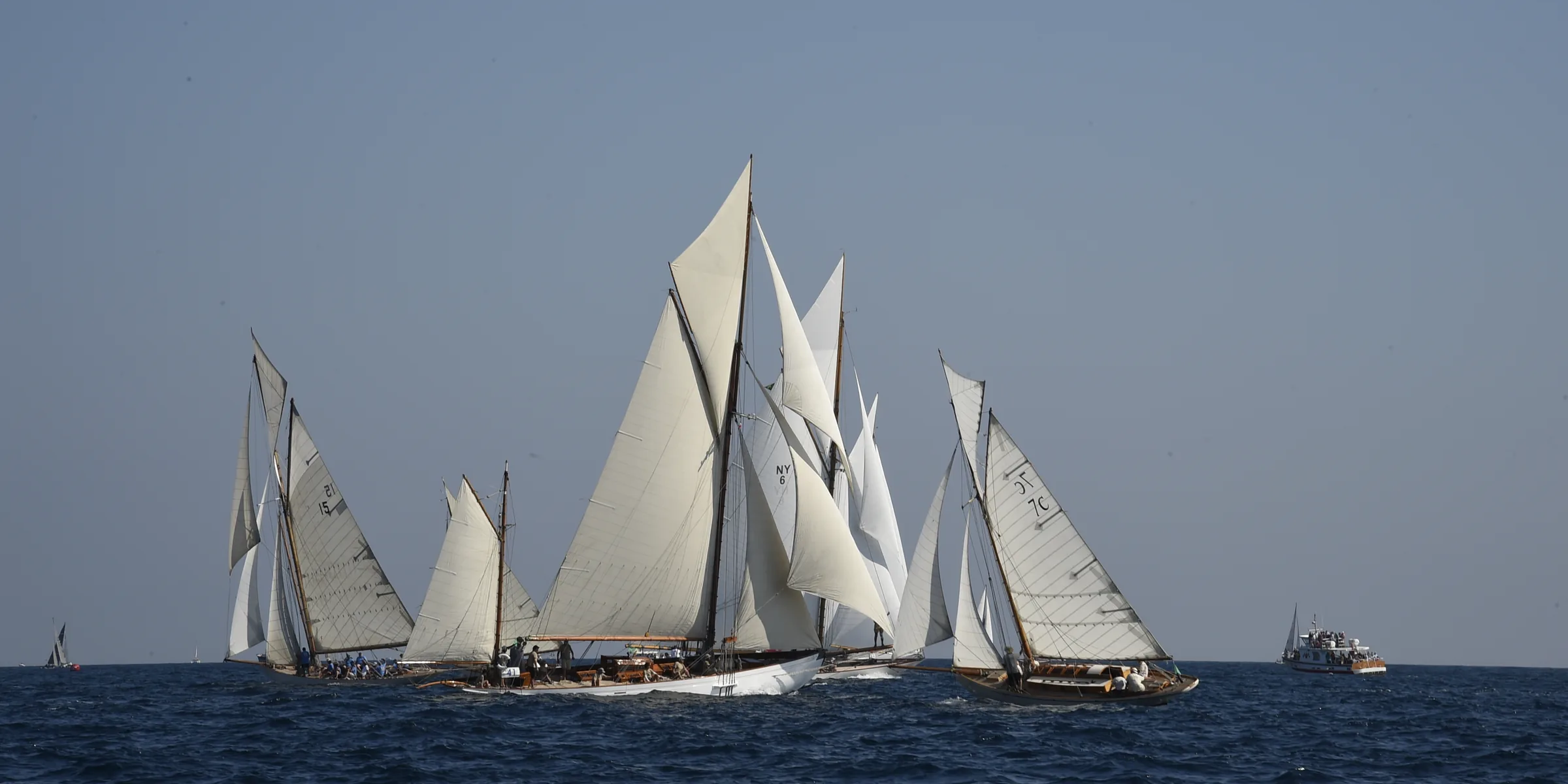 A dozen classic yachts sailing close-hauled in the gulf of Saint-Tropez under a clear sky.