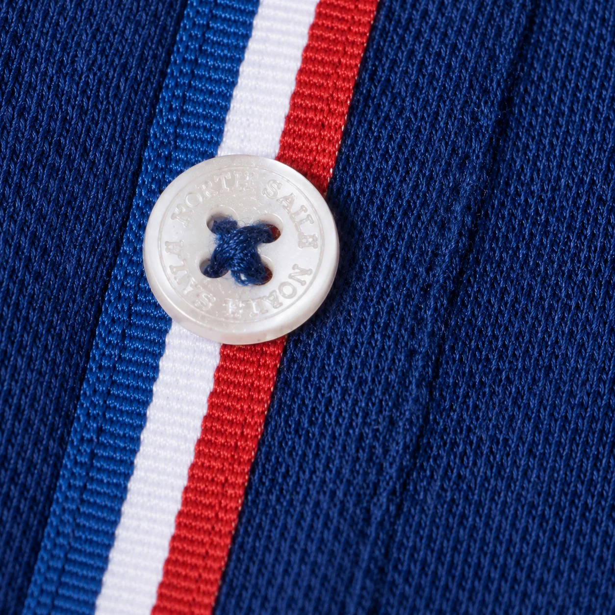 Close-up of a mother-of-pearl button stamped North Sails, sewn onto the blue-white-red tape of the button placket.