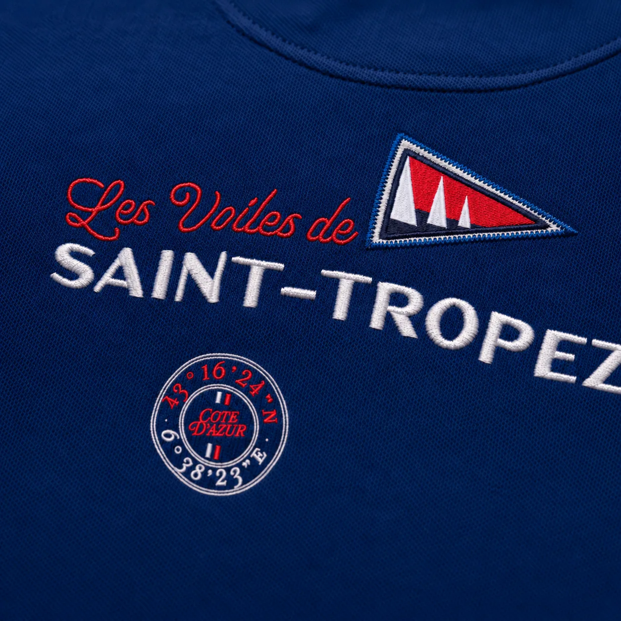 Close-up of the back embroidery below the neck: “Les Voiles de Saint-Tropez” and the coordinates of the gulf, on navy piqué knit.