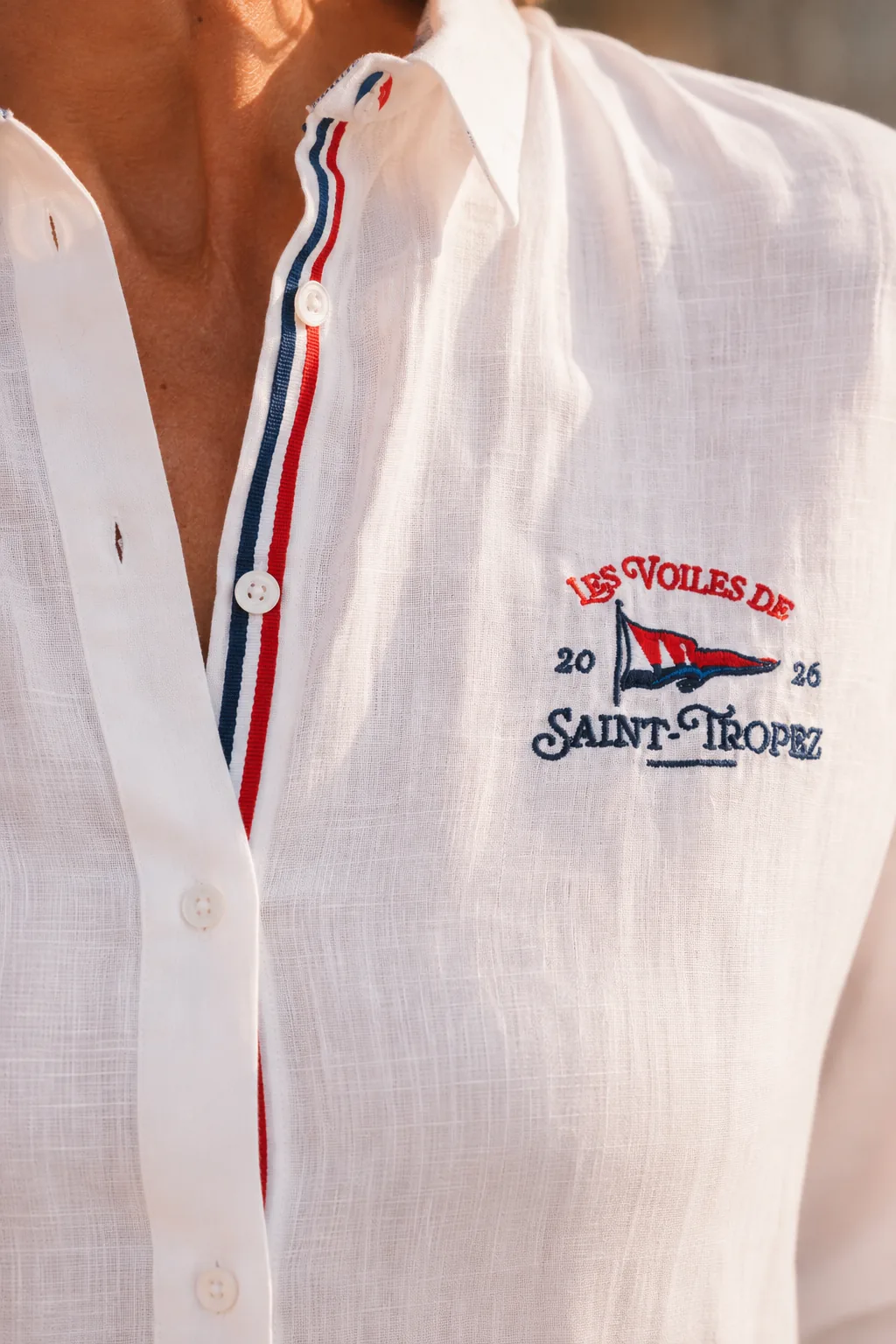Close-up of the women's linen shirt collar: tricolour tape along the button placket and pennant embroidery.