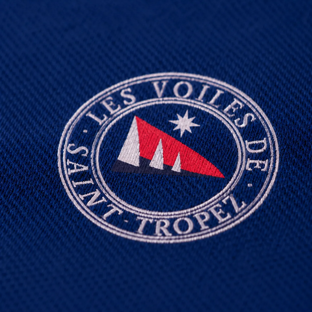 Close-up of the embroidered round badge: red pennant and white star, ringed with “Les Voiles de Saint-Tropez”.