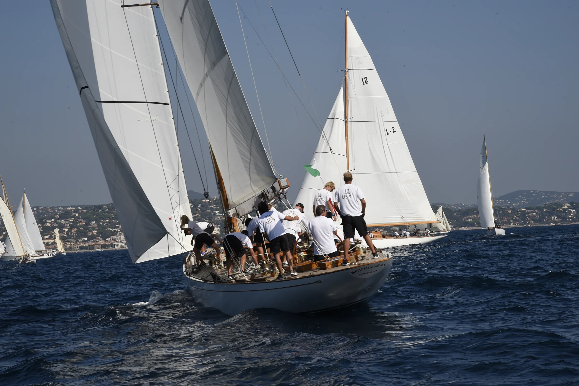 Crew hiking out on a classic yacht sailing close-hauled during the regatta, the fleet in the background.