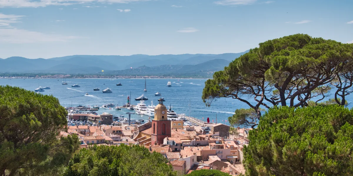 The harbour and bell tower of Saint-Tropez seen from above, the bay full of moored boats.