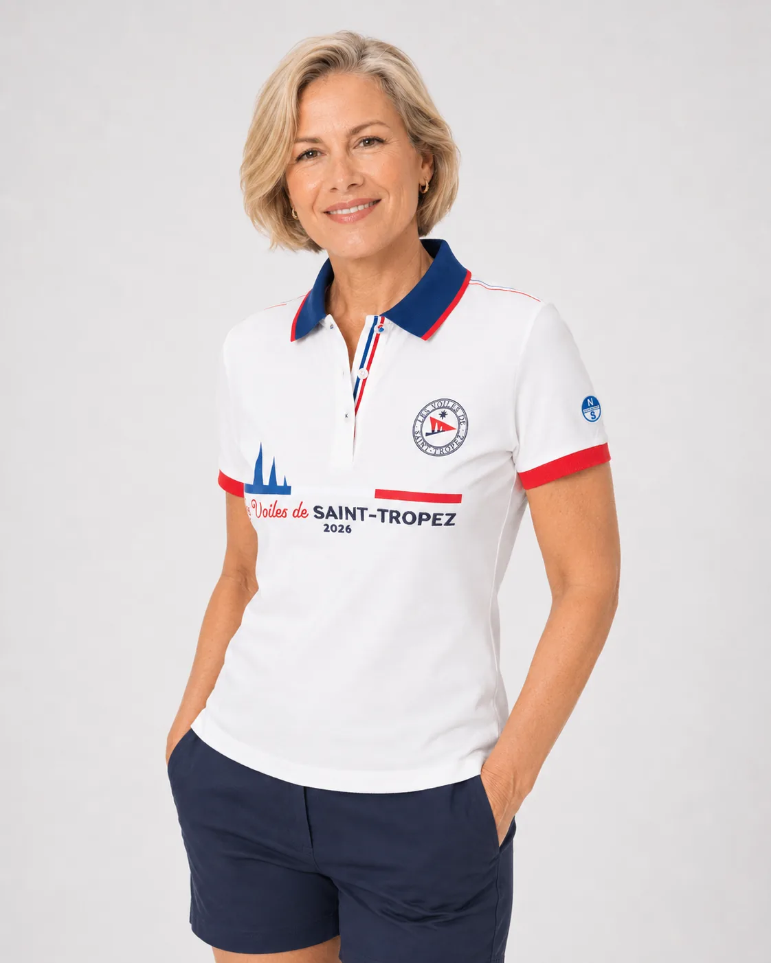 Polo Édition Limitée 26 in off-white worn from the front: navy collar with red trim, round badge, red cuffs and Les Voiles de Saint-Tropez 2026 set large across the chest.