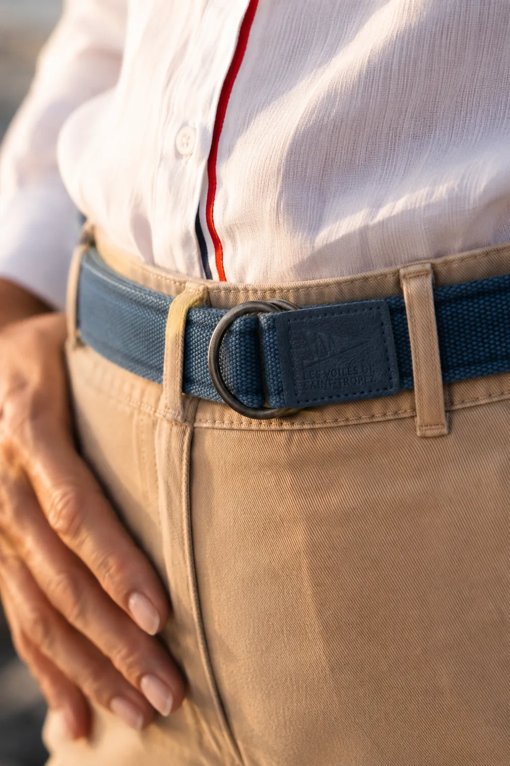 Close-up of a blue canvas belt with a double D-ring buckle, the end tab stamped Les Voiles de Saint-Tropez.