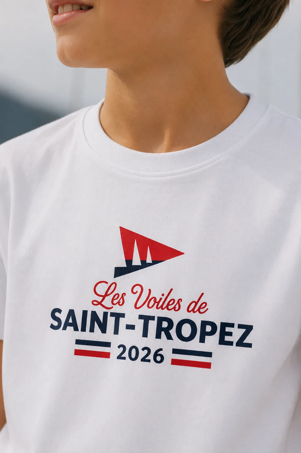 Close-up of the print on a white children's T-shirt: a red and navy burgee and “Les Voiles de Saint-Tropez 2026”.